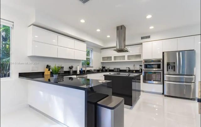 kitchen featuring light tile patterned floors, stainless steel appliances, white cabinets, island range hood, and kitchen peninsula