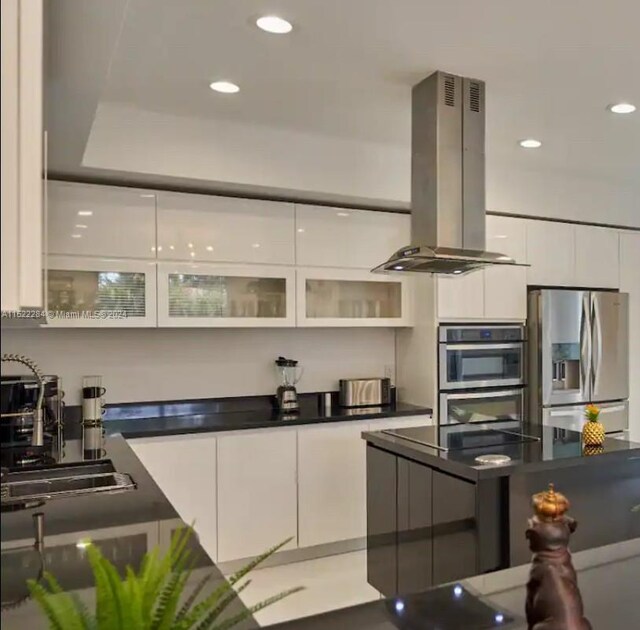 kitchen with white cabinets, dark countertops, appliances with stainless steel finishes, glass insert cabinets, and island exhaust hood