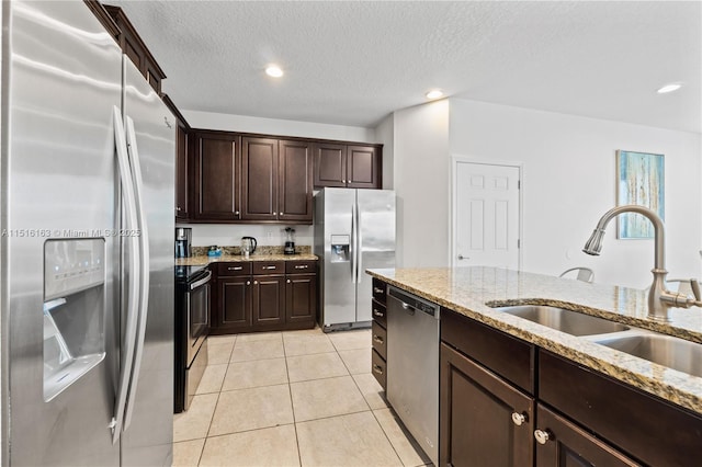 kitchen with dark brown cabinetry, sink, stainless steel appliances, and light stone countertops