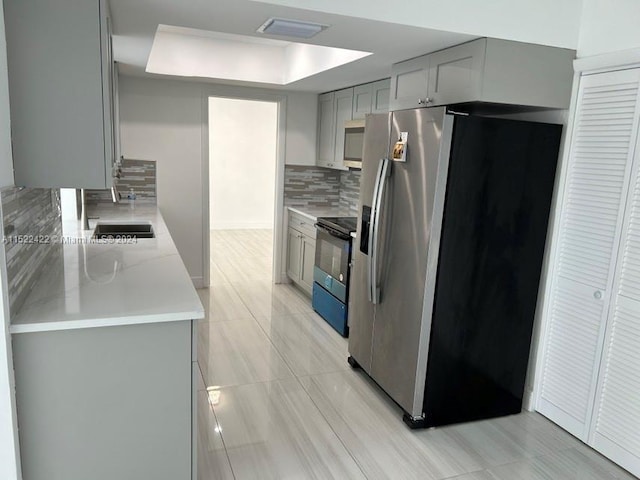 kitchen featuring a tray ceiling, backsplash, sink, stainless steel appliances, and gray cabinets