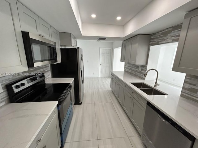 kitchen with backsplash, gray cabinets, appliances with stainless steel finishes, and sink