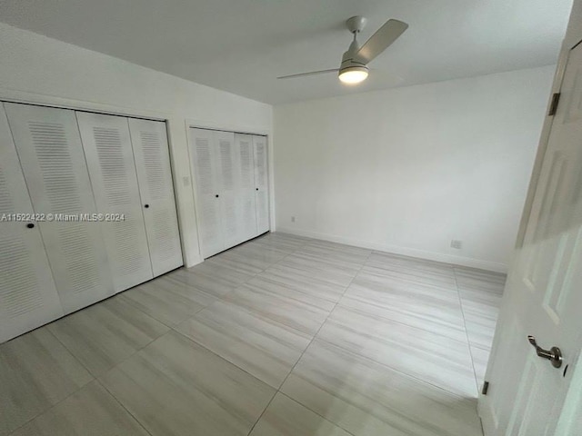 unfurnished bedroom featuring light tile floors, ceiling fan, and multiple closets