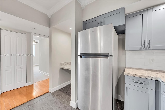 kitchen with light wood-type flooring, gray cabinets, stainless steel refrigerator, and light stone counters