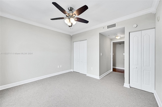 unfurnished bedroom featuring ceiling fan, carpet floors, two closets, and ornamental molding