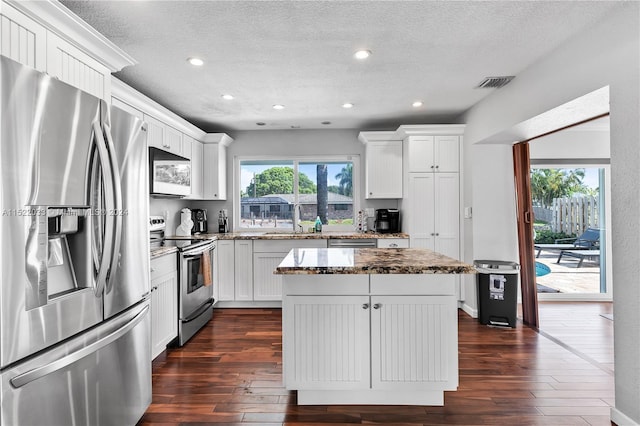 kitchen with dark hardwood / wood-style floors, a kitchen island, stainless steel appliances, stone counters, and white cabinetry