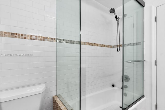 bathroom with shower / bath combination with glass door, toilet, and tile walls