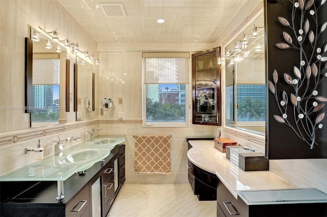 bathroom featuring dual sinks, vanity with extensive cabinet space, a healthy amount of sunlight, and tile walls