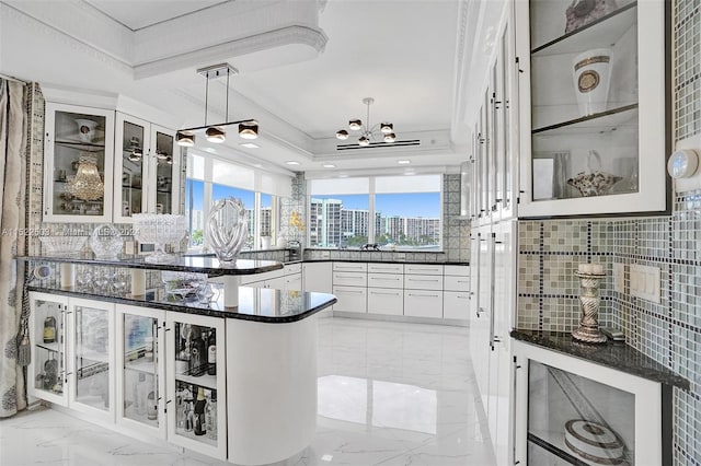 kitchen with a chandelier, pendant lighting, ornamental molding, white cabinets, and a tray ceiling