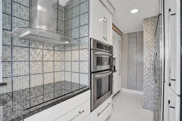 kitchen with white cabinetry, light tile flooring, appliances with stainless steel finishes, dark stone countertops, and wall chimney exhaust hood