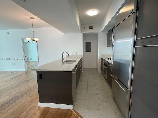 kitchen featuring built in appliances, sink, hanging light fixtures, light tile flooring, and a notable chandelier