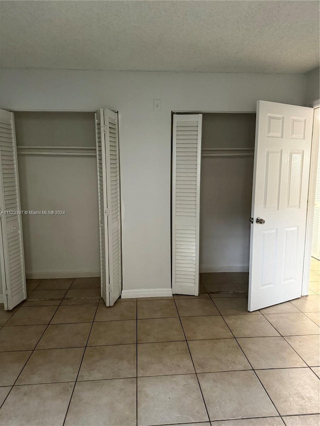 unfurnished bedroom featuring tile flooring, two closets, and a textured ceiling