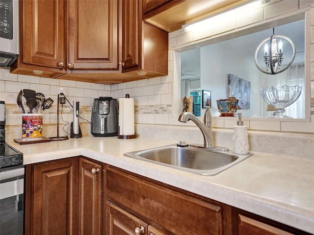 kitchen with an inviting chandelier, range, tasteful backsplash, and sink