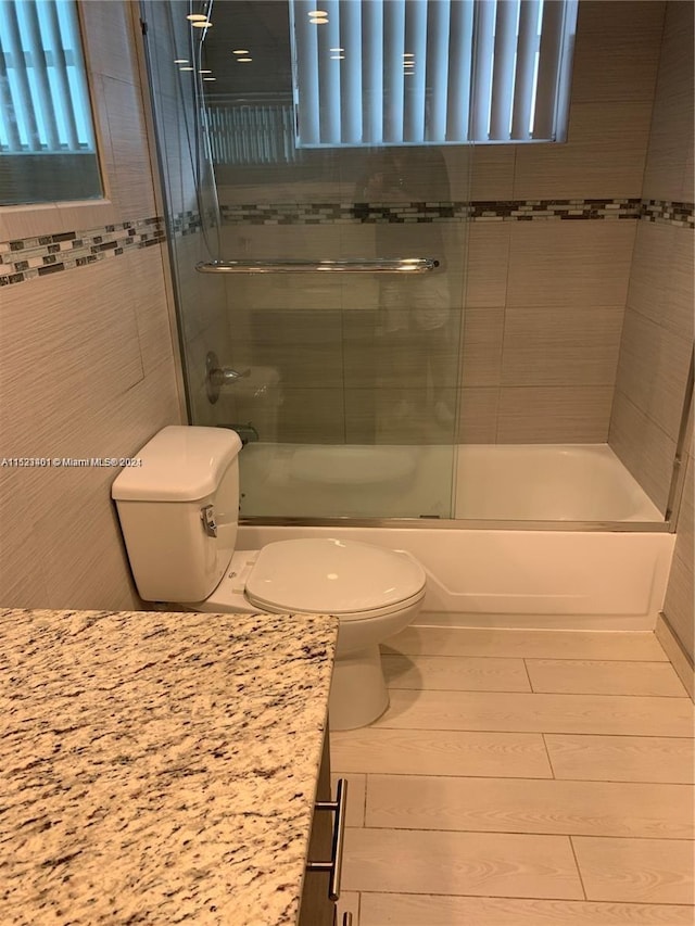 full bathroom featuring tile walls, toilet, bath / shower combo with glass door, and vanity