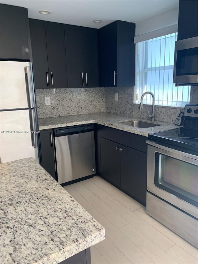 kitchen featuring backsplash, light stone countertops, stainless steel appliances, and sink