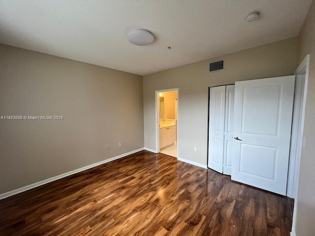 unfurnished bedroom featuring ensuite bath, a closet, a textured ceiling, and dark hardwood / wood-style flooring