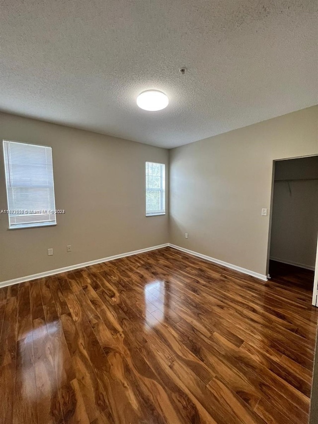 unfurnished room with a textured ceiling and dark wood-type flooring