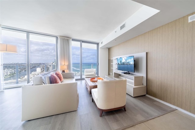 living room with floor to ceiling windows, a water view, and light wood-type flooring