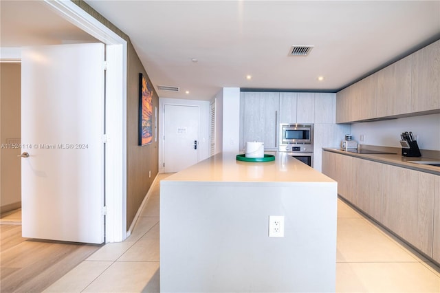 kitchen with light tile flooring, light brown cabinetry, a kitchen island, and appliances with stainless steel finishes