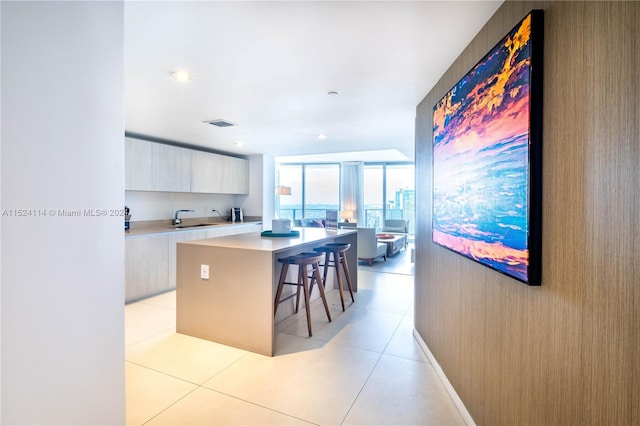 kitchen featuring a wall of windows, sink, light tile floors, a kitchen island, and a kitchen bar