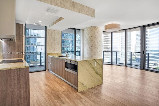 kitchen featuring black electric cooktop, floor to ceiling windows, light hardwood / wood-style flooring, sink, and light stone counters