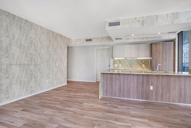 kitchen with sink, white cabinetry, light stone countertops, and light wood-type flooring