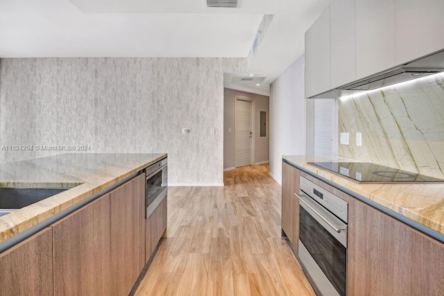 kitchen featuring light wood-type flooring, light stone countertops, stainless steel appliances, and white cabinetry