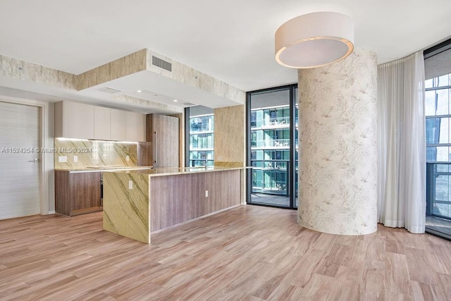 kitchen with light stone countertops, floor to ceiling windows, light hardwood / wood-style flooring, white cabinets, and backsplash