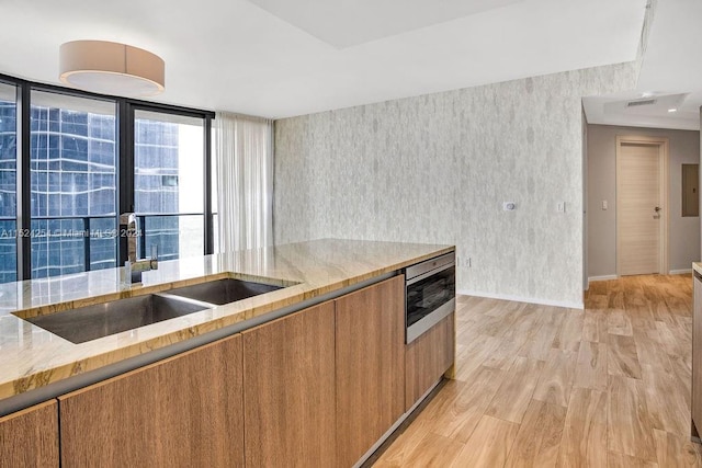 kitchen with expansive windows, light stone countertops, light hardwood / wood-style floors, and sink