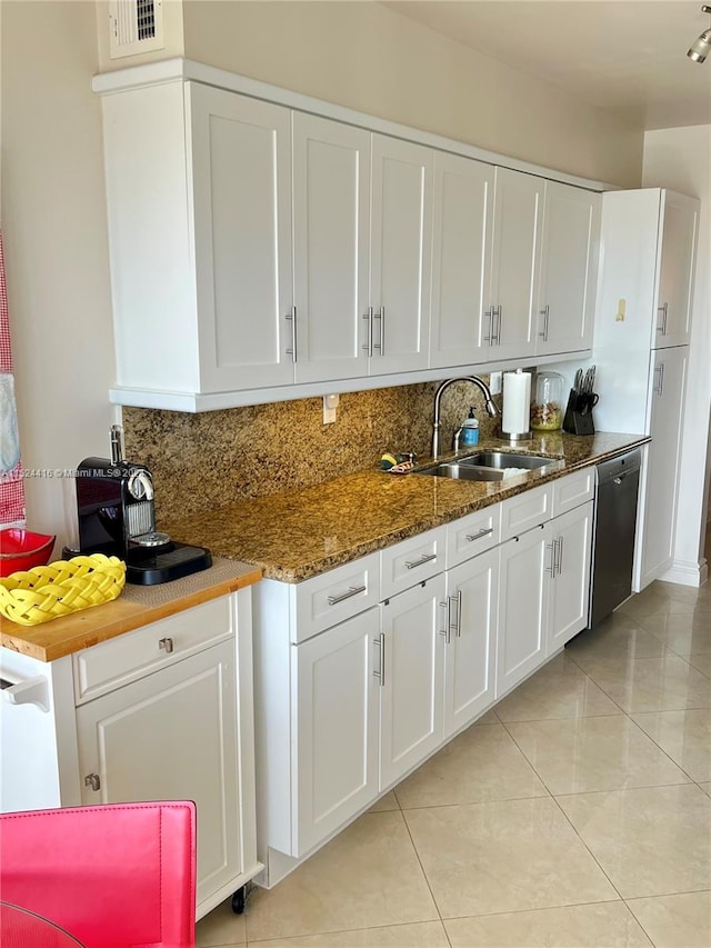 kitchen featuring dark stone counters, sink, stainless steel dishwasher, light tile patterned floors, and white cabinetry