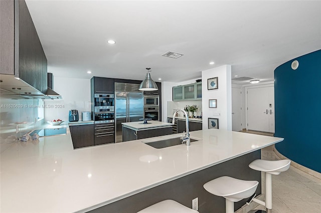 kitchen featuring sink, light tile floors, hanging light fixtures, a center island with sink, and wall chimney exhaust hood