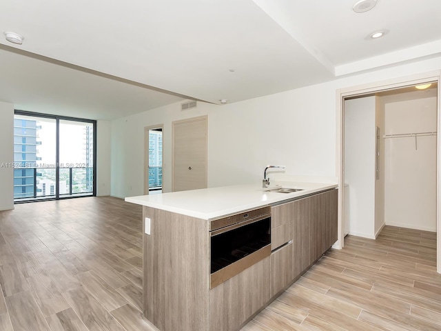 kitchen with stainless steel oven, floor to ceiling windows, light hardwood / wood-style floors, and sink