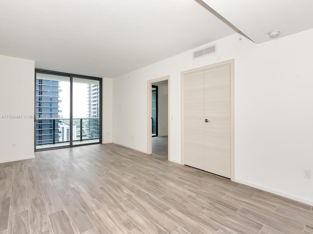 empty room with floor to ceiling windows and light hardwood / wood-style flooring