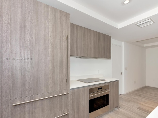 kitchen featuring oven, light brown cabinets, black electric cooktop, and light hardwood / wood-style flooring