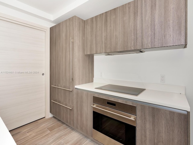 kitchen featuring light hardwood / wood-style floors, black electric stovetop, stainless steel oven, and light brown cabinetry