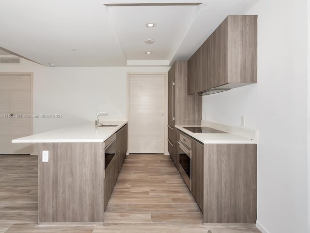 kitchen featuring black electric stovetop, stainless steel oven, sink, and light wood-type flooring