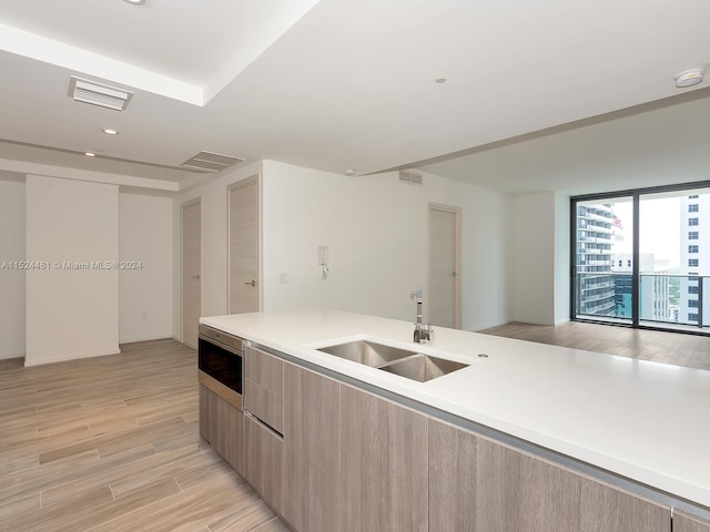 kitchen featuring a wall of windows, stainless steel microwave, sink, and light hardwood / wood-style flooring