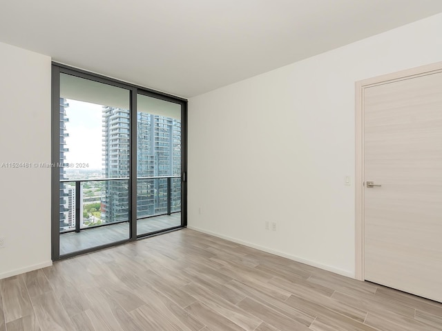 unfurnished room with floor to ceiling windows and light hardwood / wood-style flooring