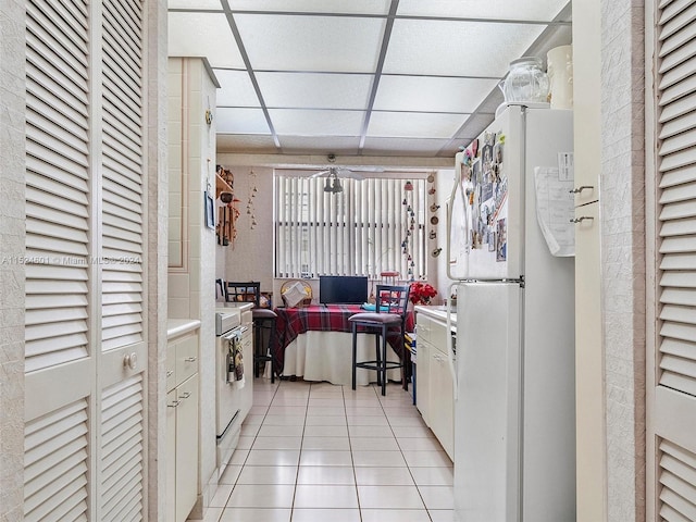 kitchen featuring decorative light fixtures, white cabinetry, light tile floors, a drop ceiling, and white refrigerator