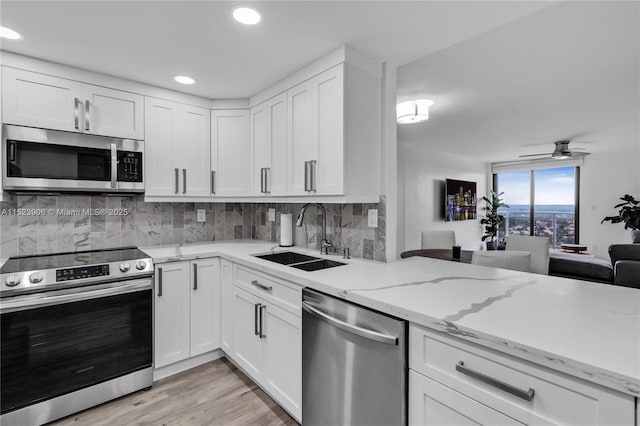 kitchen featuring light wood-style flooring, a sink, tasteful backsplash, appliances with stainless steel finishes, and white cabinets