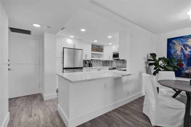 kitchen featuring light wood-style flooring, light stone counters, white cabinetry, stainless steel appliances, and decorative backsplash