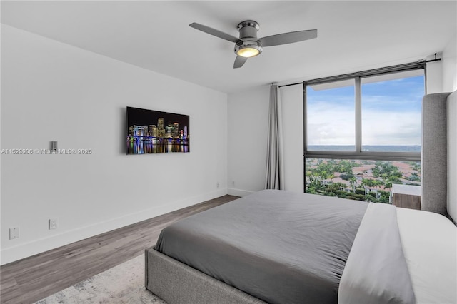 bedroom with floor to ceiling windows, a ceiling fan, baseboards, and wood finished floors