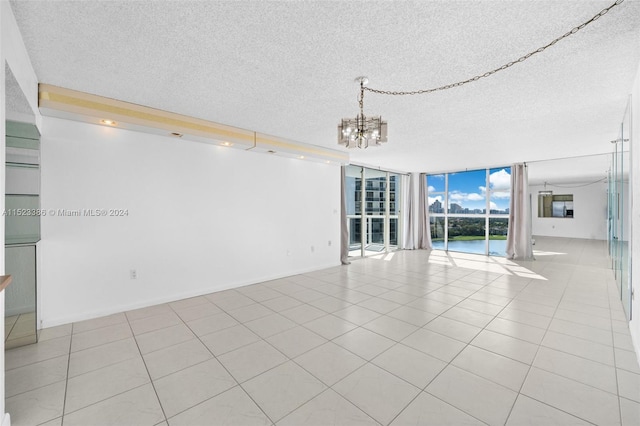 spare room featuring a notable chandelier, light tile patterned floors, a textured ceiling, and expansive windows