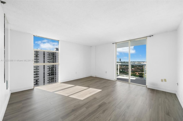 unfurnished room featuring a wall of windows, dark hardwood / wood-style flooring, and a textured ceiling