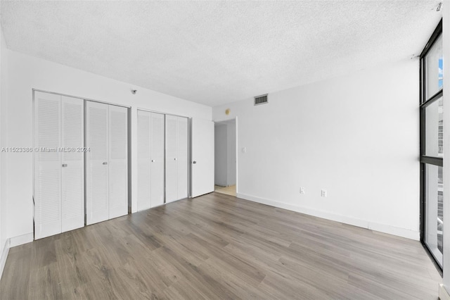 unfurnished bedroom featuring wood-type flooring, two closets, and a textured ceiling