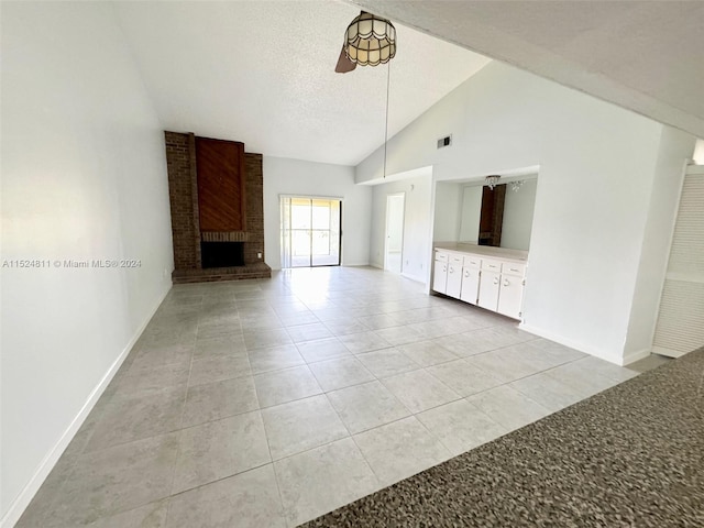 unfurnished living room featuring ceiling fan, brick wall, a brick fireplace, light tile floors, and a textured ceiling