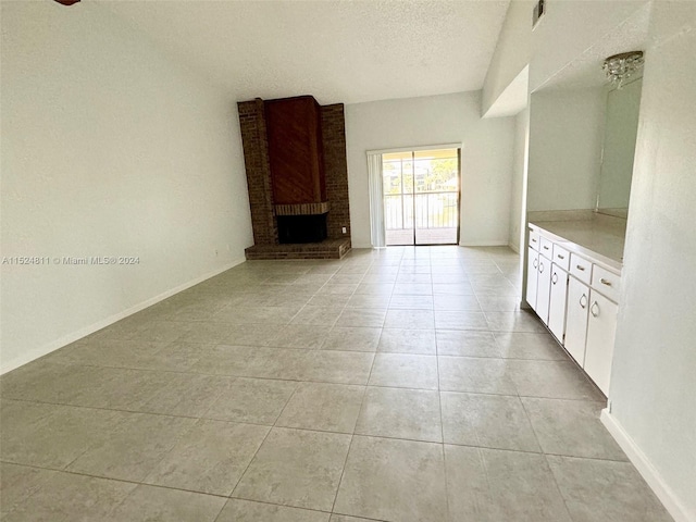 interior space featuring light tile floors, a textured ceiling, brick wall, and a brick fireplace