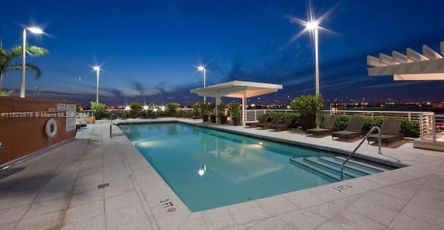 pool at dusk with a pergola and a patio area