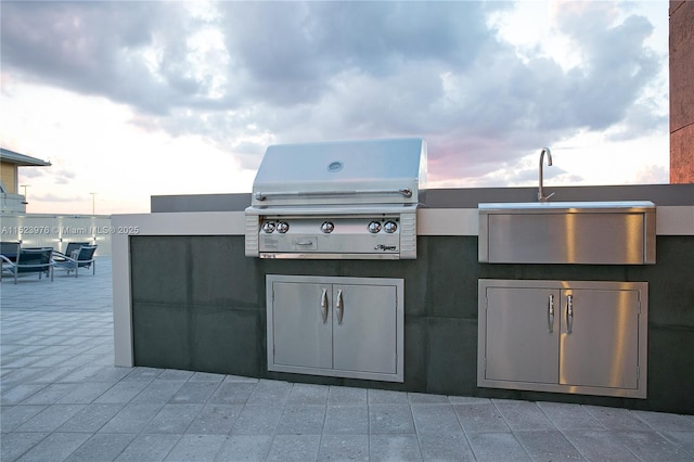 patio terrace at dusk featuring area for grilling, exterior kitchen, and sink