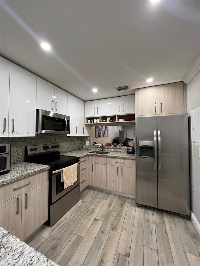 kitchen with stainless steel appliances, light brown cabinetry, light hardwood / wood-style flooring, light stone counters, and sink