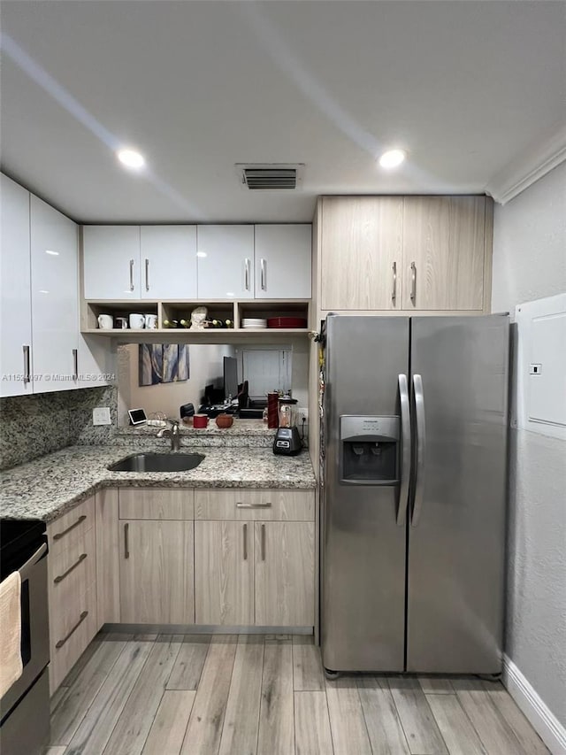 kitchen featuring light stone countertops, stainless steel fridge, sink, and light wood-type flooring